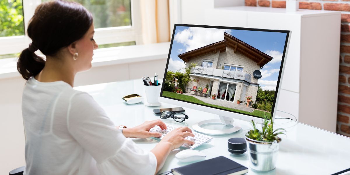 Woman sitting at a desk looking at a house photo on a computer screen.